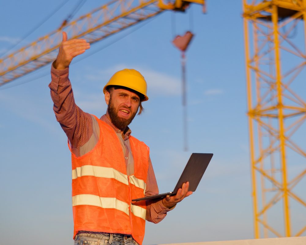 Construction engineer using laptop at building site with crane in background
